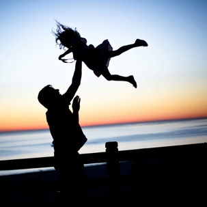 silhouette of father tossing daughter in front of ocean sunset, Photo by lauren lulu taylor on Unsplash